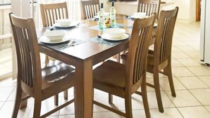 A dining table set with plates, cutlery, and bottles, surrounded by wooden chairs in a well-lit room with tiled flooring. - Rye Sleeps 10, Great Weekender (Rye)