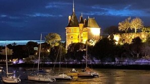 Un edificio parecido a un castillo con múltiples torres, rodeado de árboles y una masa de agua con barcos.
