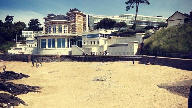 Un hotel frente al mar con una playa arenosa, ventanas amplias y una torre destacada.