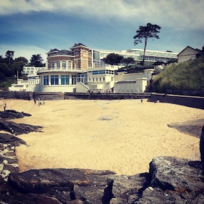 A coastal hotel with a sandy beach, large windows, and a prominent tower structure.