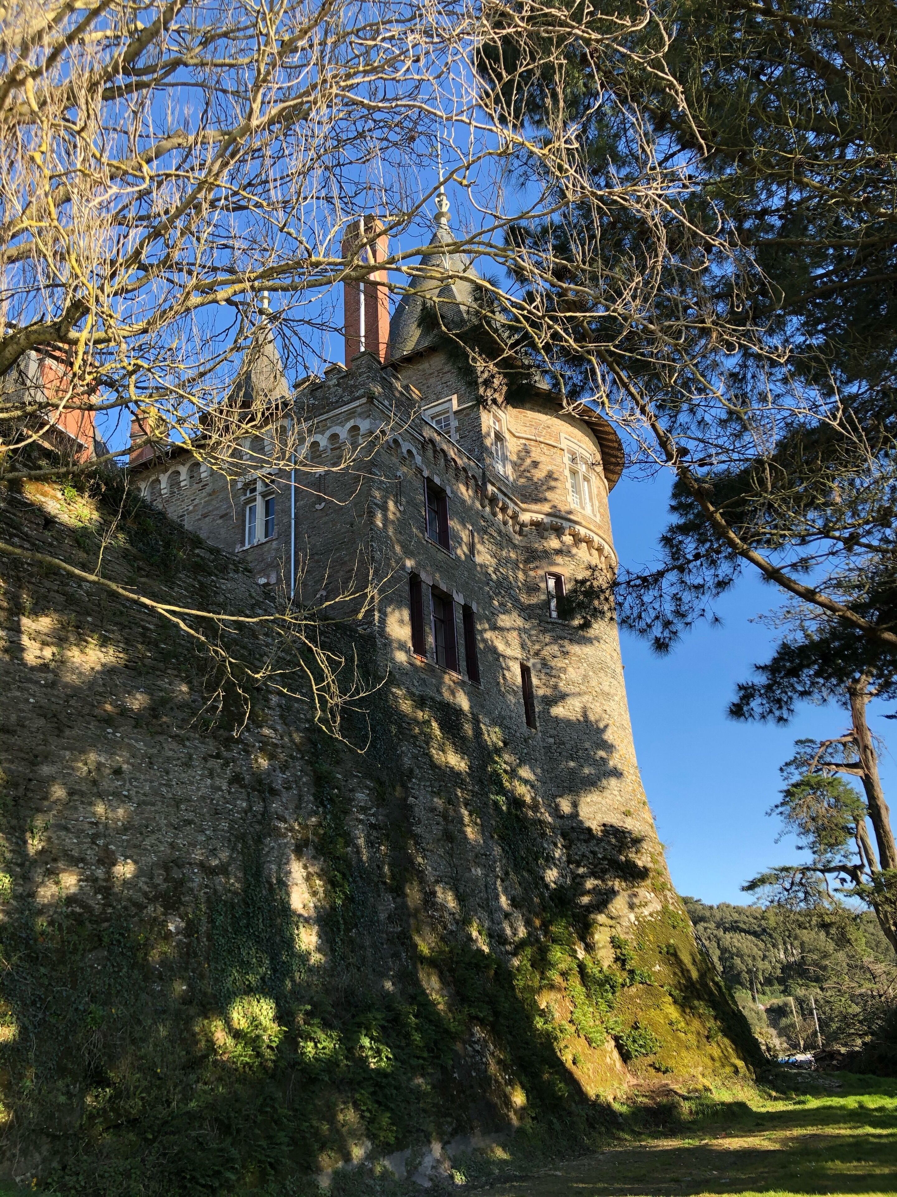 A historic stone tower with arched windows and a dome, surrounded by trees and a clear sky.