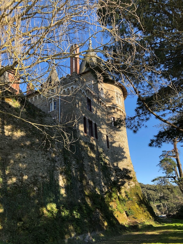 A historic stone tower with arched windows and a dome, surrounded by trees and a clear sky.