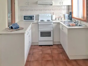 Efficient kitchen with microwave, stove, and sink, featuring white cabinetry and a tiled backsplash.