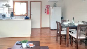 A compact kitchen with a window, a dining area with wooden chairs, and a small table with a plant.