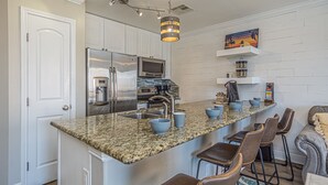 A modern kitchen with granite countertops, stainless steel appliances, and bar stools. - Coastal Comfort at Beach Barn - Pet Friendly! (Galveston)