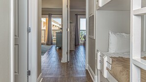 A hallway with wooden flooring, white walls, and a bunk bed on the right. - Coastal Comfort at Beach Barn - Pet Friendly! (Galveston)