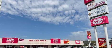 A MaxValu AEON store with multiple signs, a parking lot, and a clear sky.