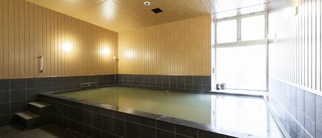 A spa room with a large bathtub, wooden walls, and a window providing natural light.