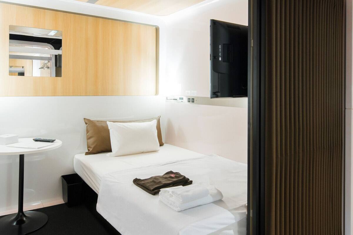 Une chambre d’hôtel comprenant un lit, une table de chevet, une petite table ronde, un miroir et un téléviseur fixé au mur.