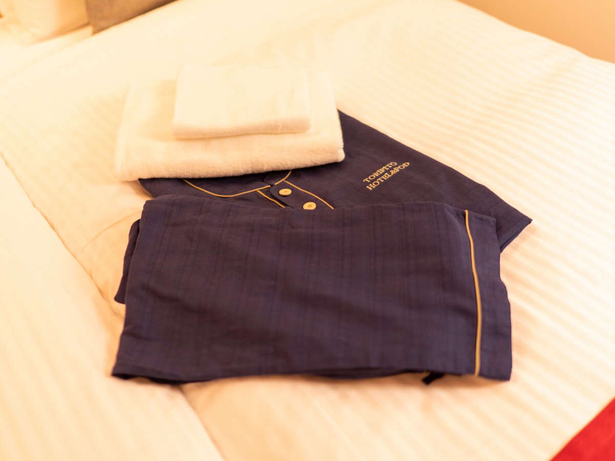 A neatly made bed with a folded towel and a dark blue garment on it.