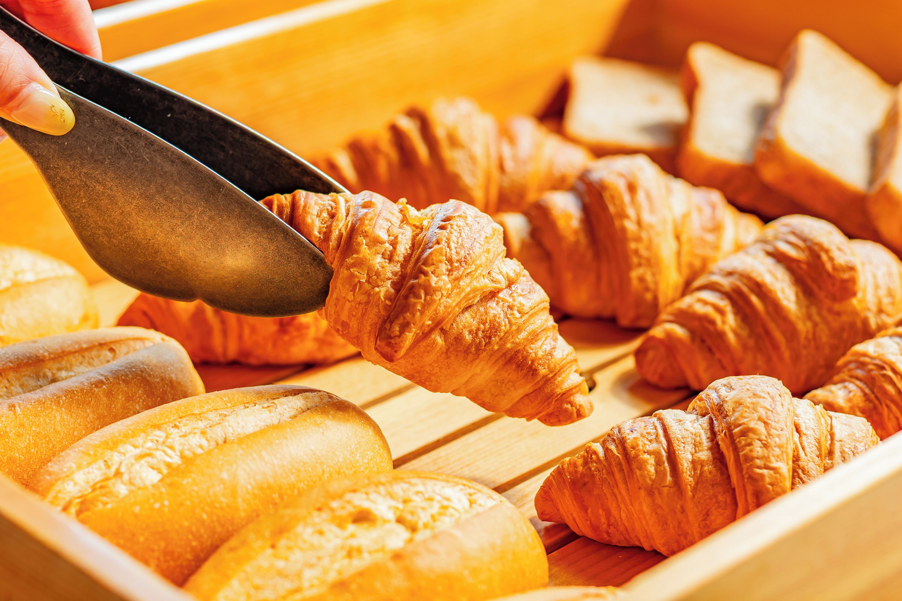 A variety of baked goods, including croissants and baguettes, displayed in a wooden tray.