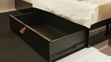 A modern hotel room with a black storage unit under the bed, a white bedspread, and a grey carpet.