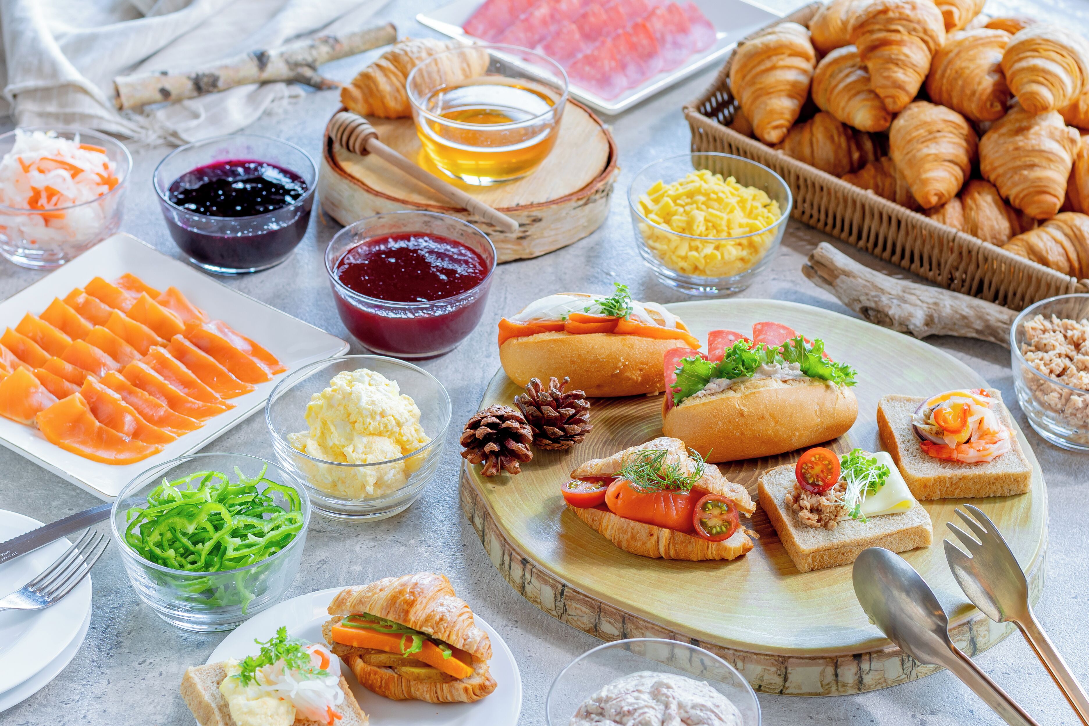 Une variété d’aliments, notamment des croissants, des sandwichs et des légumes frais, sont disposés sur une table.