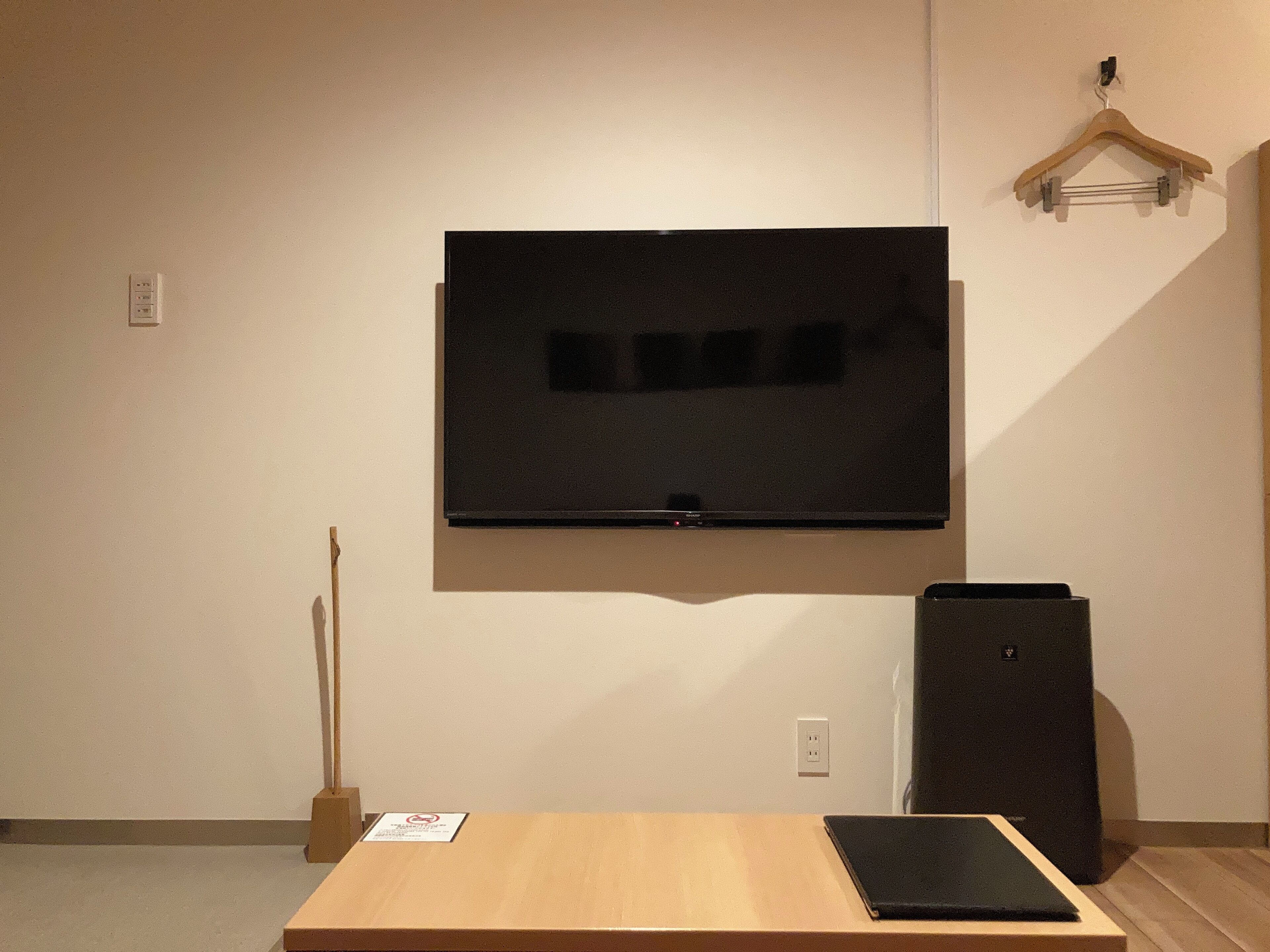 A room with a mounted flat-screen TV, a wooden table, a black speaker, and a wooden hanger on the wall.