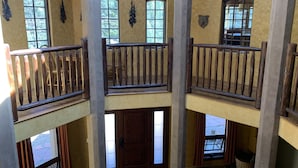 A multi-level interior with wooden railings, large windows, and a stone fireplace.