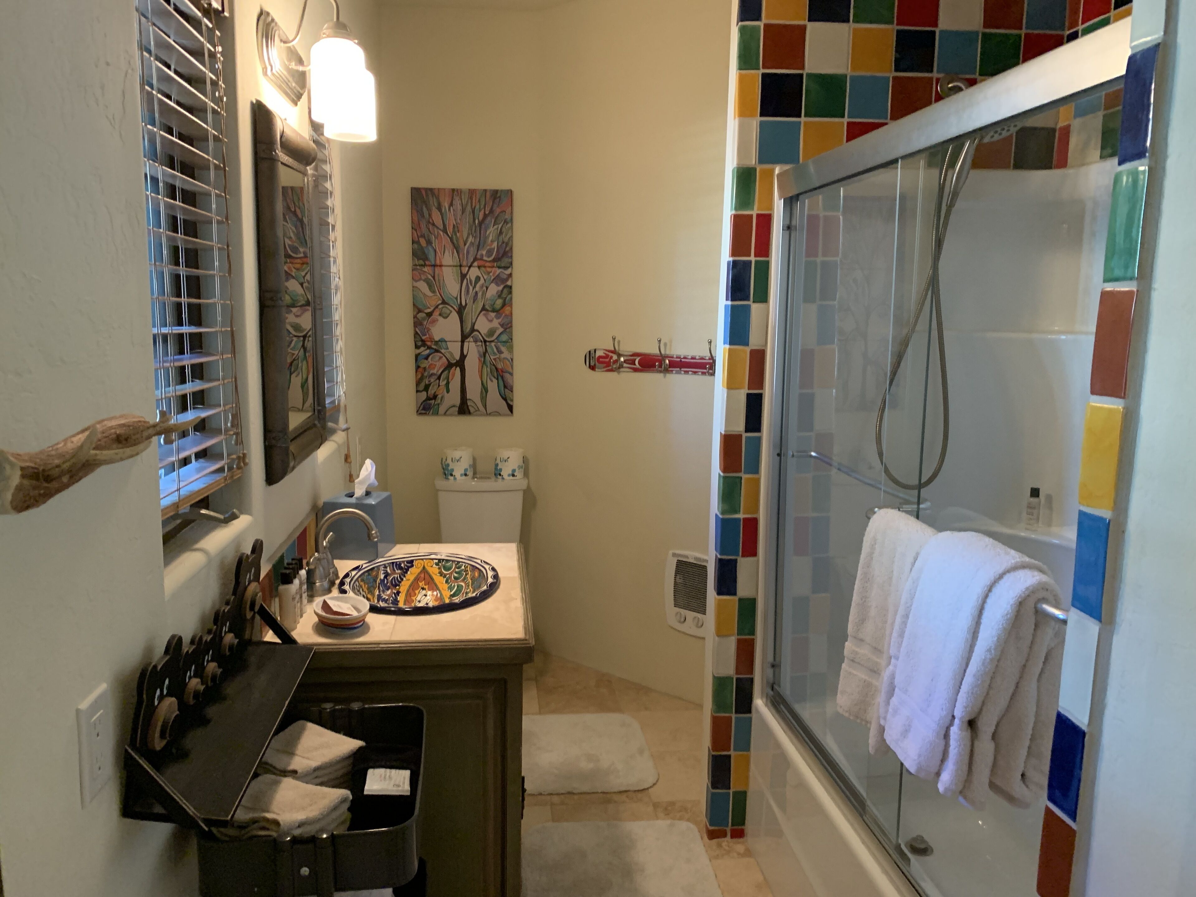 Un bagno con doccia, un lavandino con una ciotola decorativa, un portascopevoli e uno schienale colorato in piastrelle.