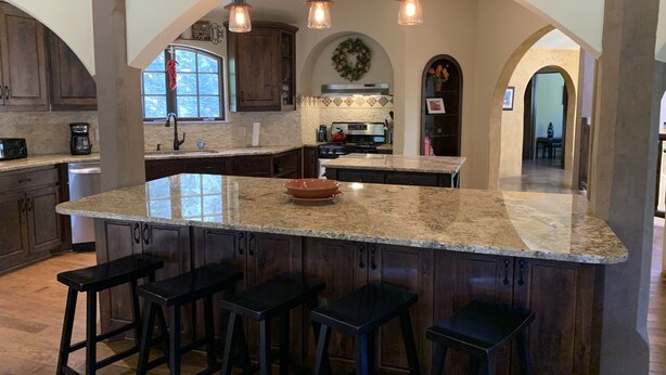A spacious kitchen with a large island, dark wooden cabinets, and a central archway.