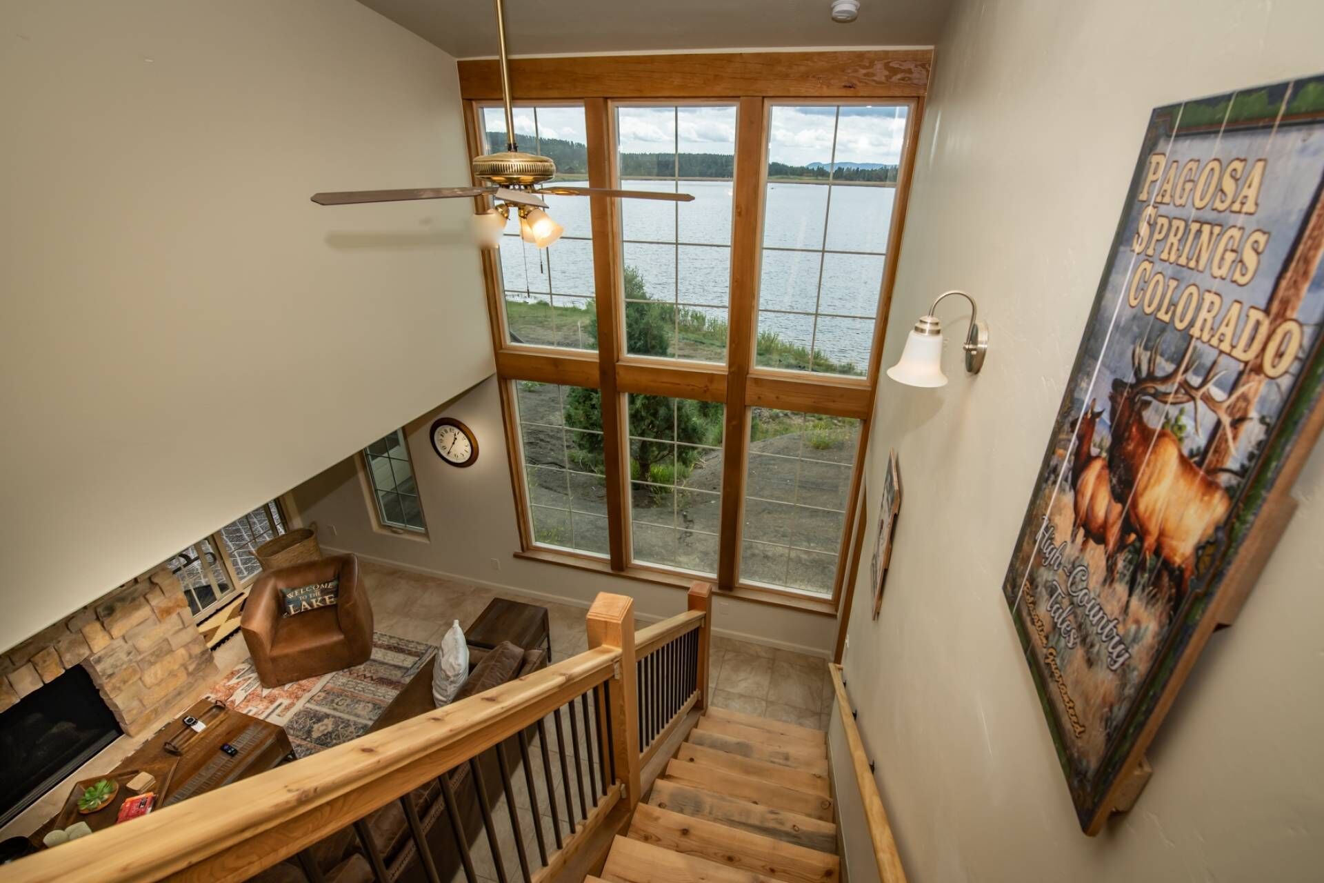 Un escalier menant à une pièce d’où l’on peut admirer la vue sur un lac, avec une horloge et une affiche représentant un élan.