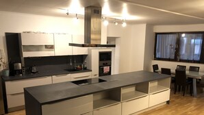 A modern kitchen with a central island, built-in appliances, and a dining area with a view. - Pension Günther (Graz)