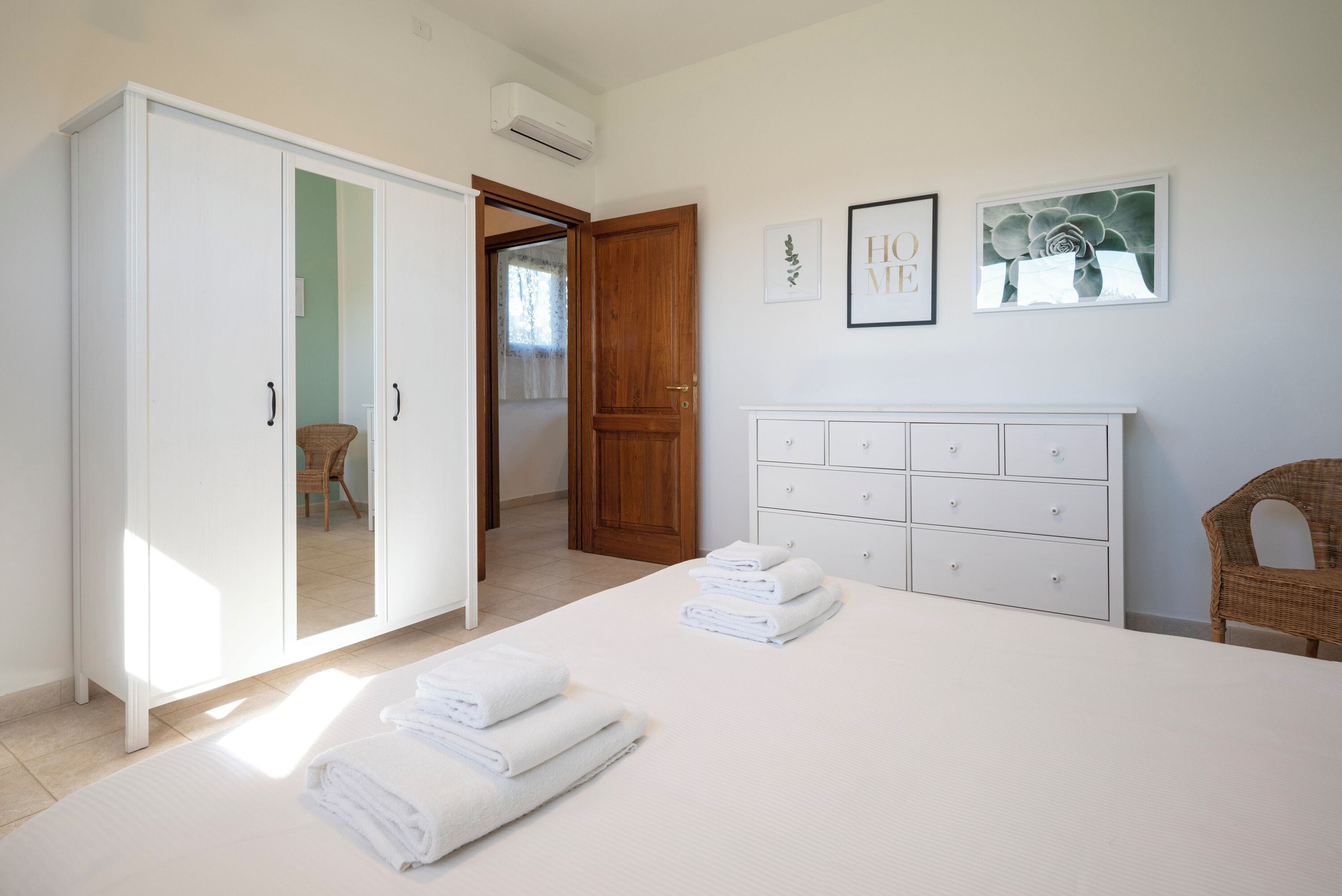 Een slaapkamer met een bed, een kledingkast, een dressoir en twee foto's in lijsten aan de muur.