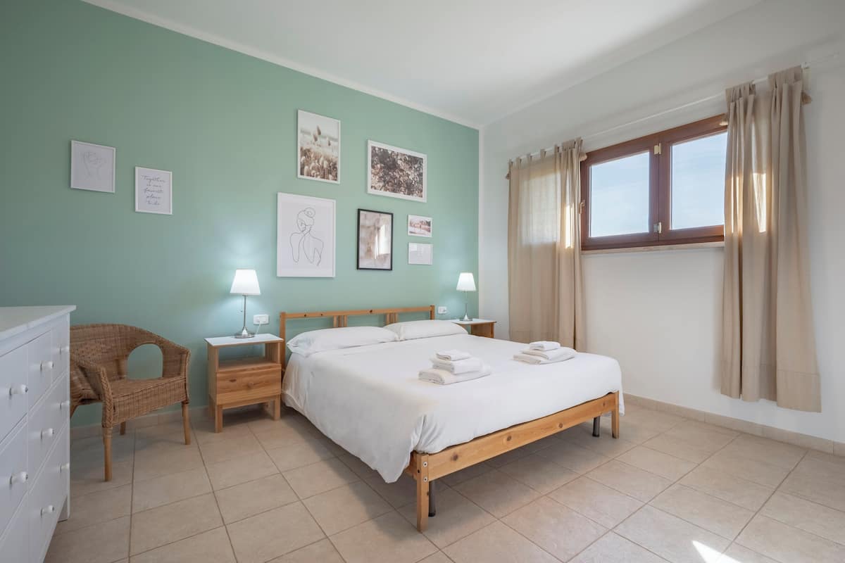 Une chambre à coucher comprenant un lit, des tables de chevet, une chaise et des œuvres d’art murales.