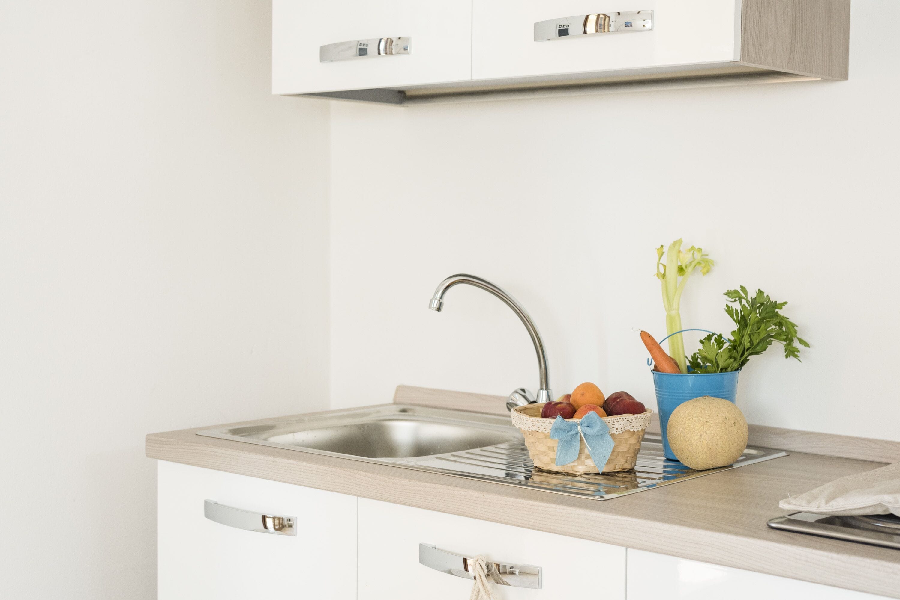 Une cuisine dotée d’un évier en acier inoxydable, d’un plan de travail en bois et de meubles blancs.