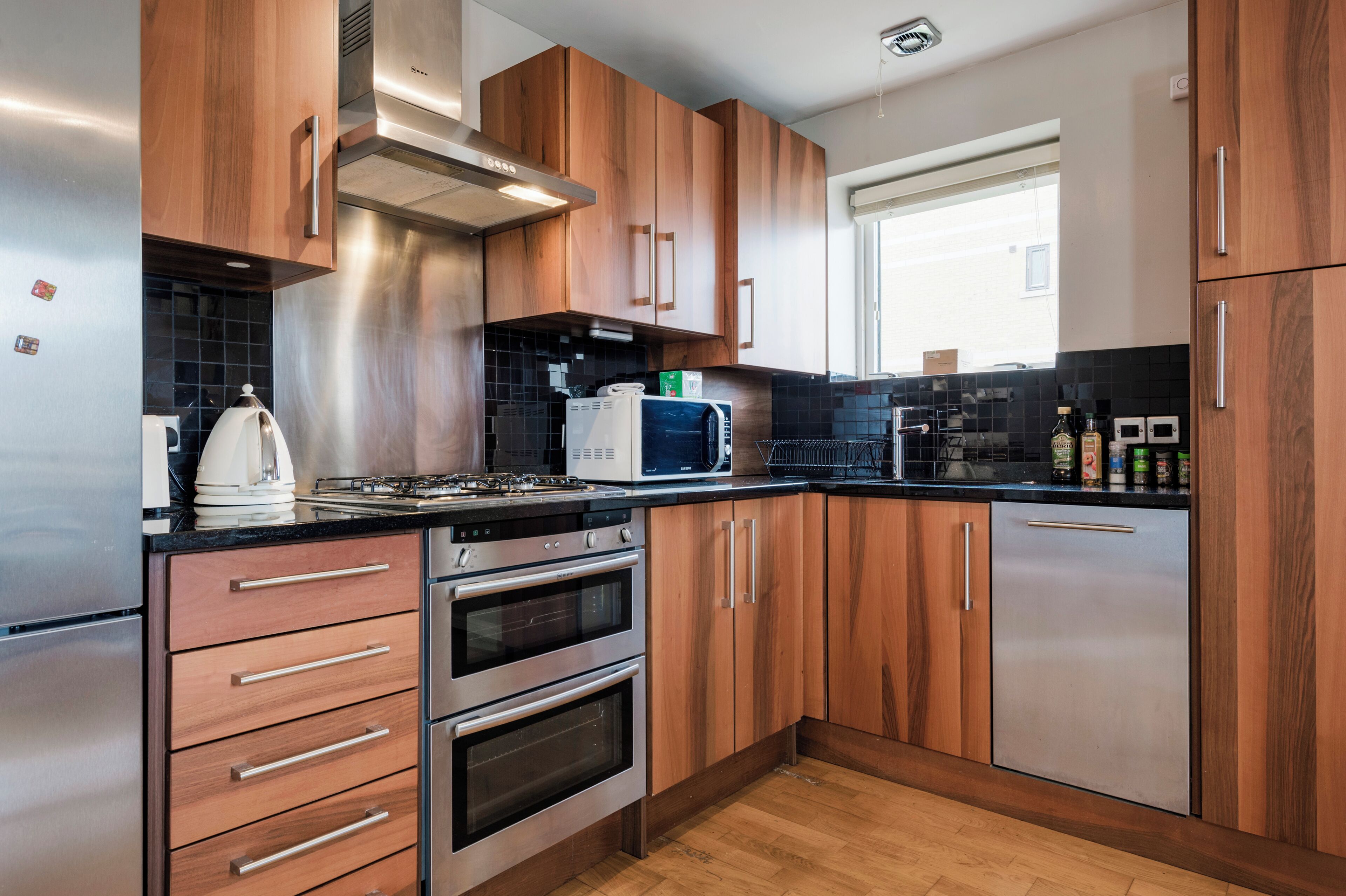 A modern kitchen with wooden cabinets, stainless steel appliances, and a black countertop.