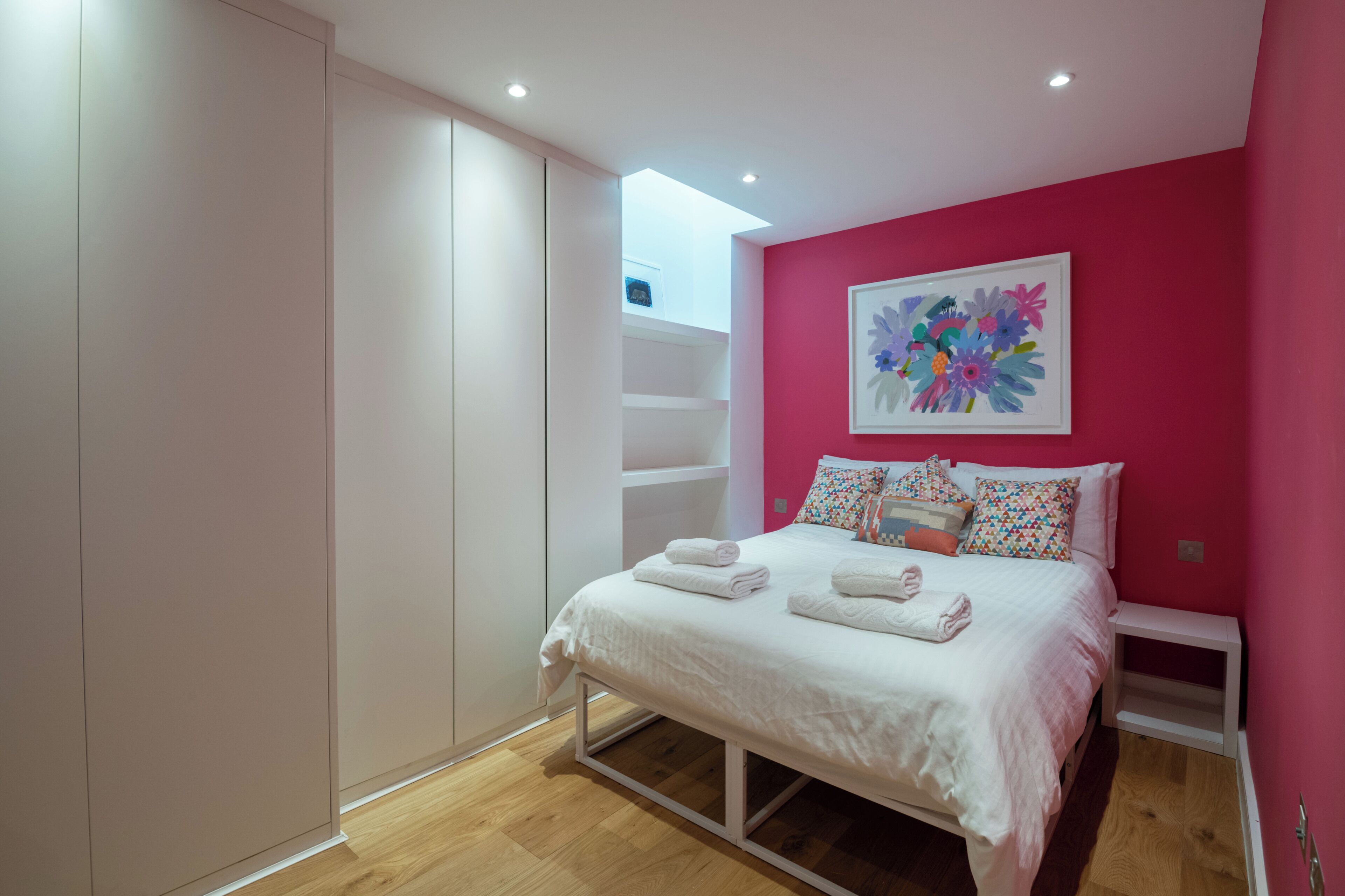 Ein Schlafzimmer mit Bett, weißem Kleiderschrank und einem farbenfrohen Bild an der Wand.