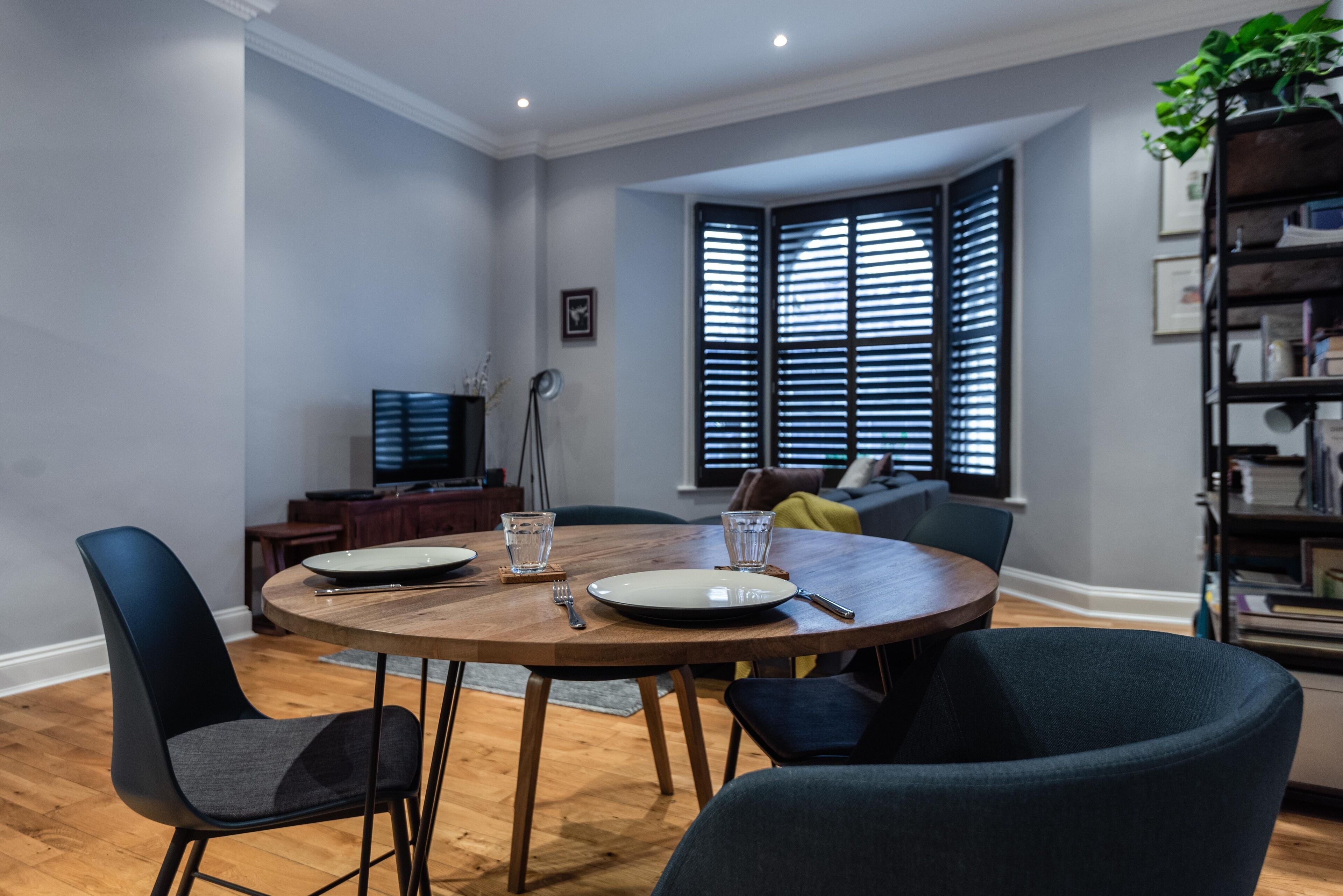 Un coin repas avec une table ronde en bois, des chaises noires et un téléviseur en arrière-plan.