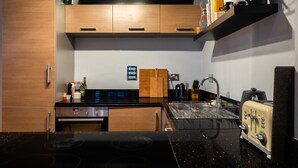 Una cuina moderna amb armaris de fusta, un taulell negre, una torradora antiga i un rentaplat amb estenedora.