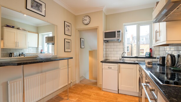A modern kitchen with white cabinets, a black countertop, a microwave, and a dishwasher. - Traditional Fulham Home Close to the River Thames by Underthedoormat (London)