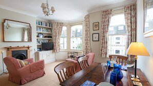 A cozy living room with a fireplace, bookshelves, a television, and a dining area with a table set for two. - Traditional Fulham Home Close to the River Thames by Underthedoormat (London)