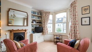 A cozy living room with a fireplace, red patterned chairs, a bookshelf, and a television. - Traditional Fulham Home Close to the River Thames by Underthedoormat (London)