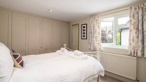 A bedroom with a bed, a wardrobe, a window with curtains, and a radiator. - Traditional Fulham Home Close to the River Thames by Underthedoormat (London)