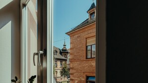 Una ventana con dos macetas de plantas en el alféizar, con vistas a una calle con edificios y un cielo despejado.