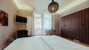 Habitación de hotel con una cama grande, un escritorio, una silla, un televisor y vistas al exterior.