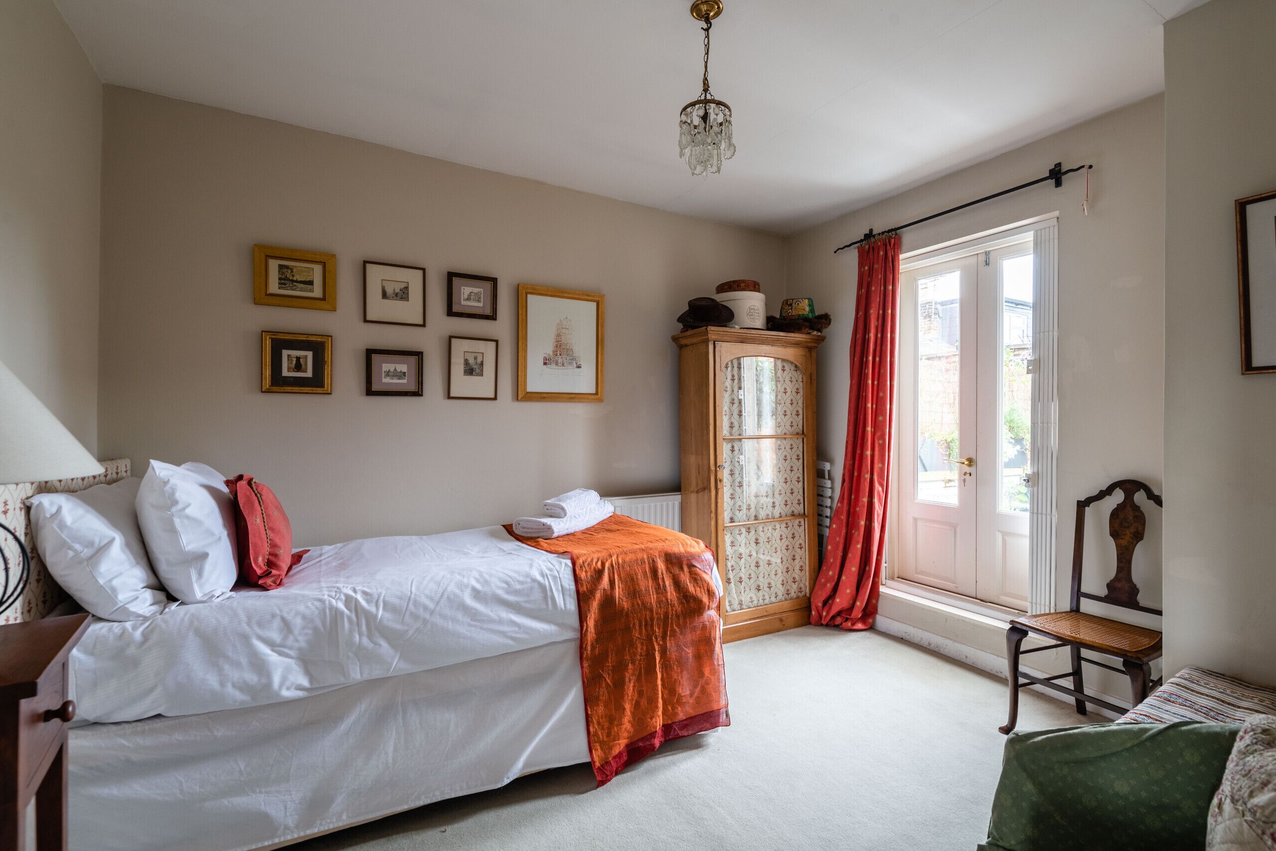 Une chambre à coucher avec un lit, une armoire en bois, une chaise et une fenêtre avec des rideaux.