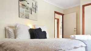 A neatly made bed with white and black bedding, a bedside table with a lamp, and a door leading to another room.