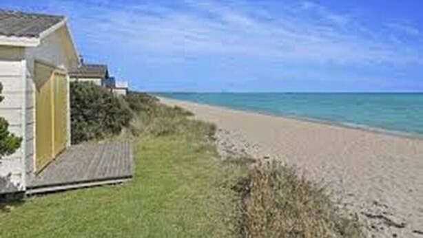 A beach house with a wooden deck and a sandy beach in the background.