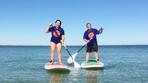Two people paddleboarding on a calm sea, wearing matching blue shirts with a logo.