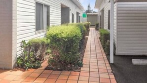 A pathway between two white buildings with a tiled walkway and green shrubbery. - Secret Dream Location with WIFI and Wine (Rye)