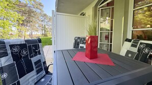 Zona de pati amb taula i dues cadires, un vas vermell i vista a un jardí.