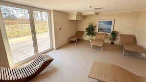 Una habitació àmplia amb un gran finestral corredísso, dues butaques, una taula petita i una planta en test.