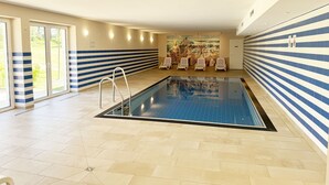 Una piscina interior amb sòl de rajola, una escala de piscina i gandules.