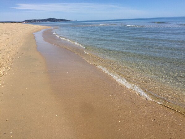 A beach with clear water, a sandy shore, and a distant hill.