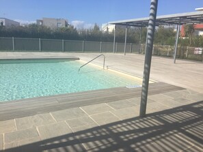 A swimming pool with clear water, surrounded by a tiled deck and metal fencing.