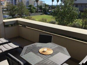 A balcony with a table, chairs, and a view of a parking lot and buildings.