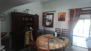 Een eetgedeelte met een tafel, stoelen, een kast met decoratieve objecten en een raam met gordijnen.
