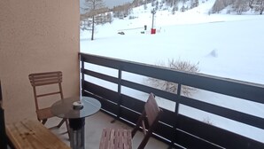 Een balkon met uitzicht op een besneeuwd landschap, een tafel en twee stoelen.