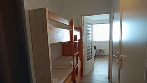 Een kamer met een stapelbed, een klein tafeltje en een deur naar een andere kamer.